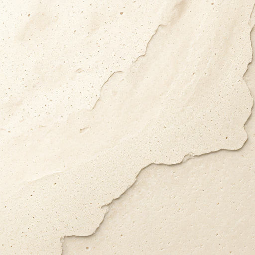 Detail of light travertine stone, its porous surface lit with soft directional light.